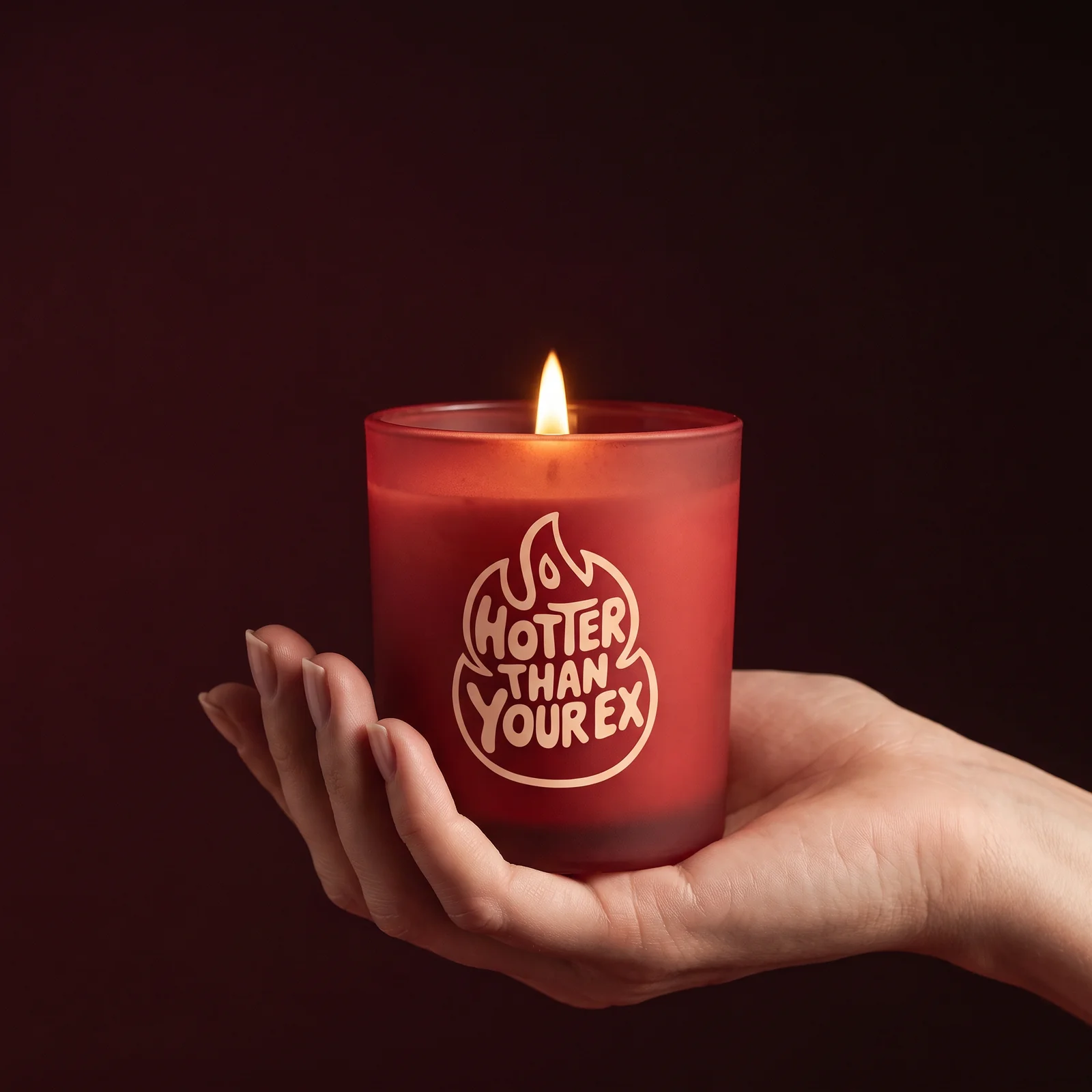 A lit red Hotter Than Your Ex candle held in an open hand against a dark red background.