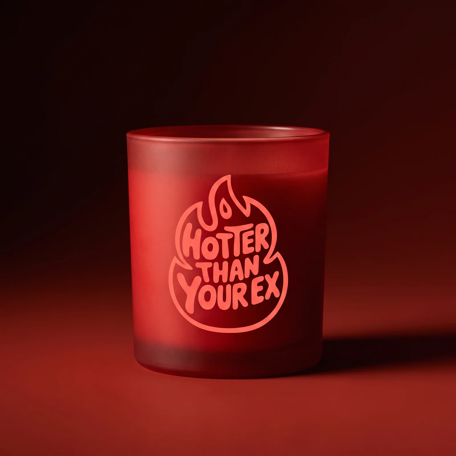 A red Hotter Than Your Ex candle with a peach flame-shaped logo against a deep red studio background.